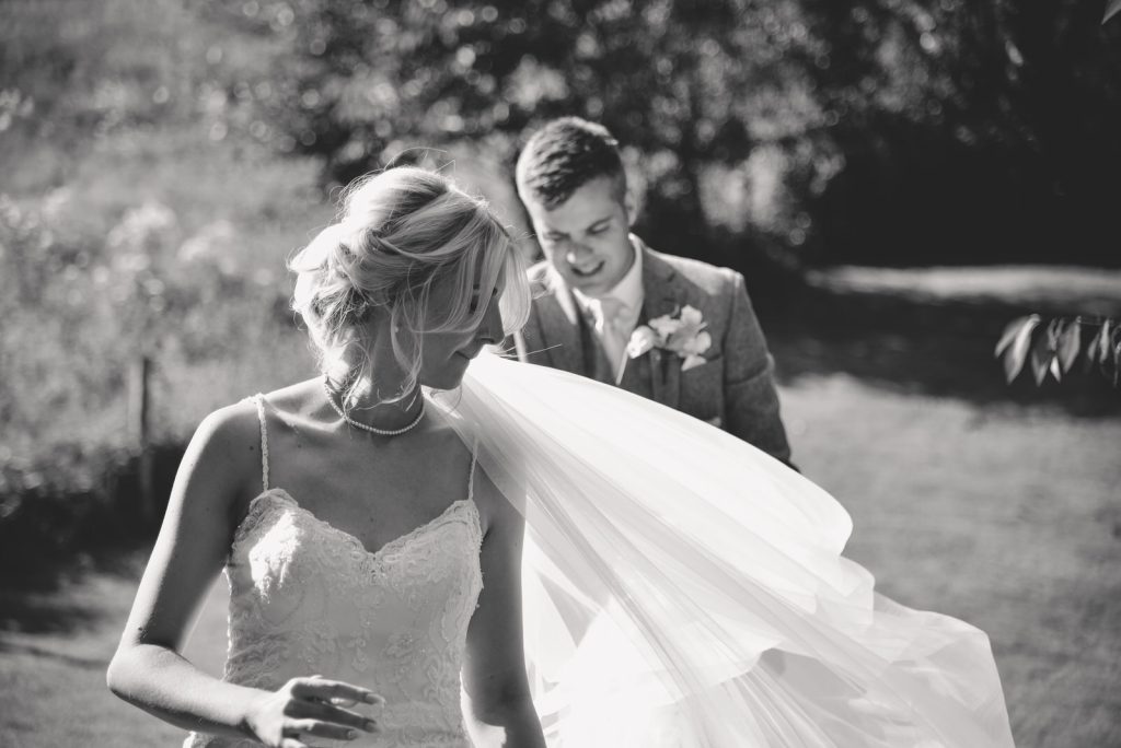 Black and white image of couple with veil blowing at The Green Cornwall captured by Memories &amp; Milestones Photography