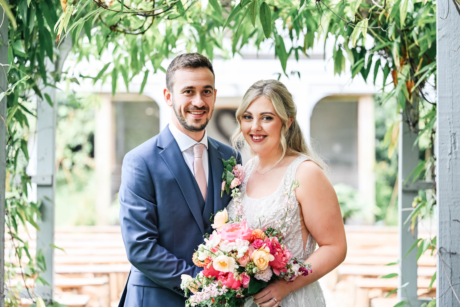 Bride and groom posing in the grounds of The Old Vicarage in Hampshire under a leafy covered walkway.